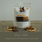 A stand-up pouch of Simmer and Co. Natural Aroma 'Be Serene Summer Mix' fragrance ingredients, displayed on a rustic wooden surface with dried orange slices, lavender buds, and cinnamon sticks.