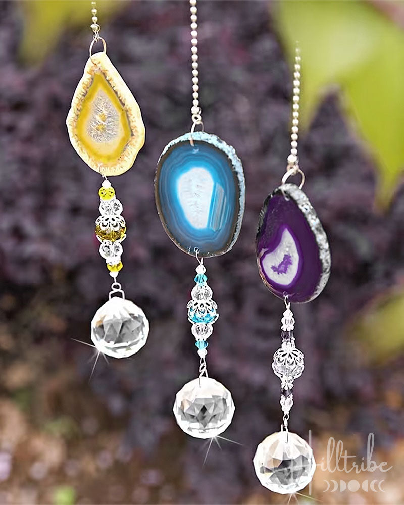 Three hanging agate slice wind chimes with clear faceted crystal pendants, shown outdoors against a blurred natural background.