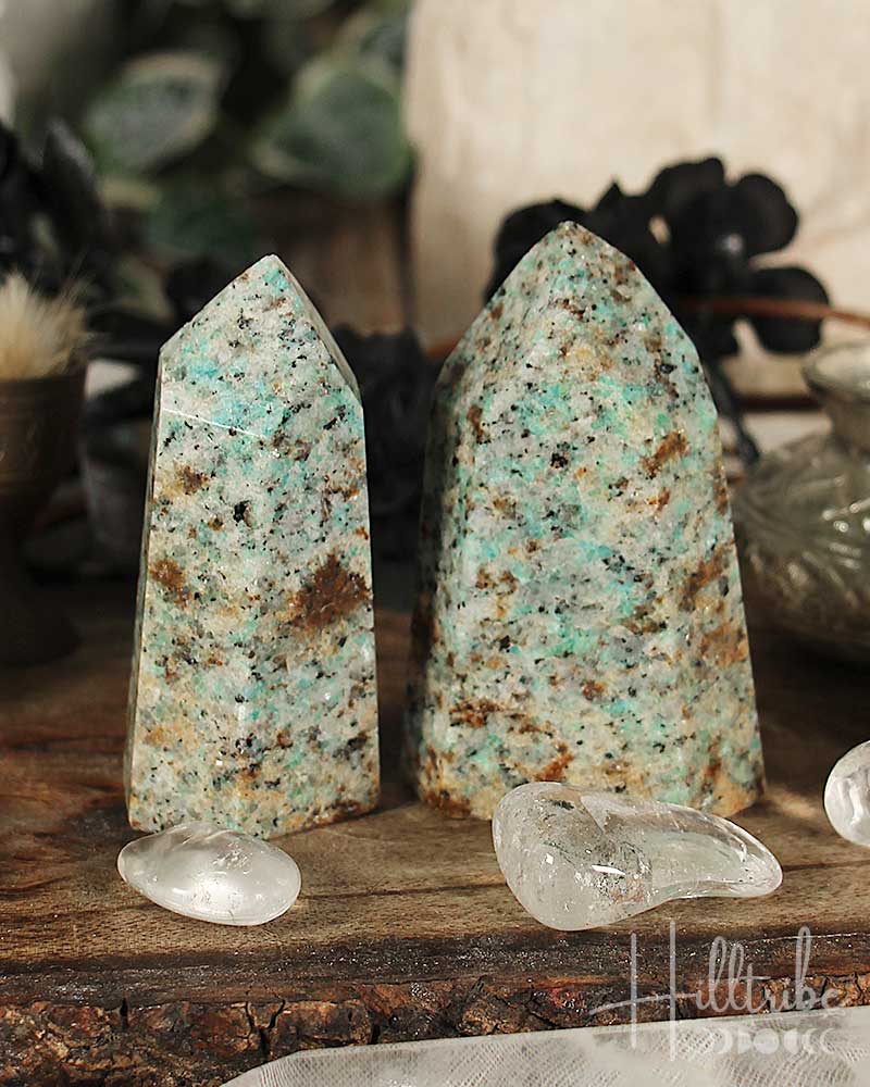 Two greenish-blue amazonite stone towers on a wooden surface with blurred background