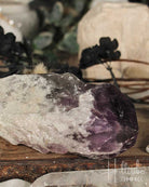 Amethyst crystal on a wooden surface with blurred plants in the background