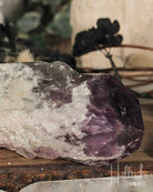 Close-up of a purple and white crystal on a wooden surface with blurred greenery in the background.