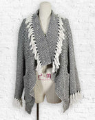 Black and white patterned shawl with fringe on a mannequin against a white brick wall.