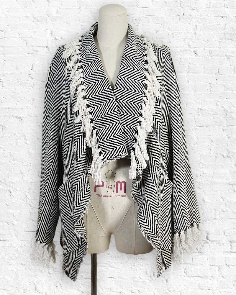 Black and white patterned shawl with fringe on a mannequin against a white brick wall.