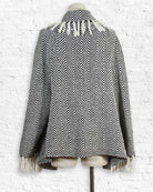 Black and white patterned poncho on a mannequin against a white brick wall.