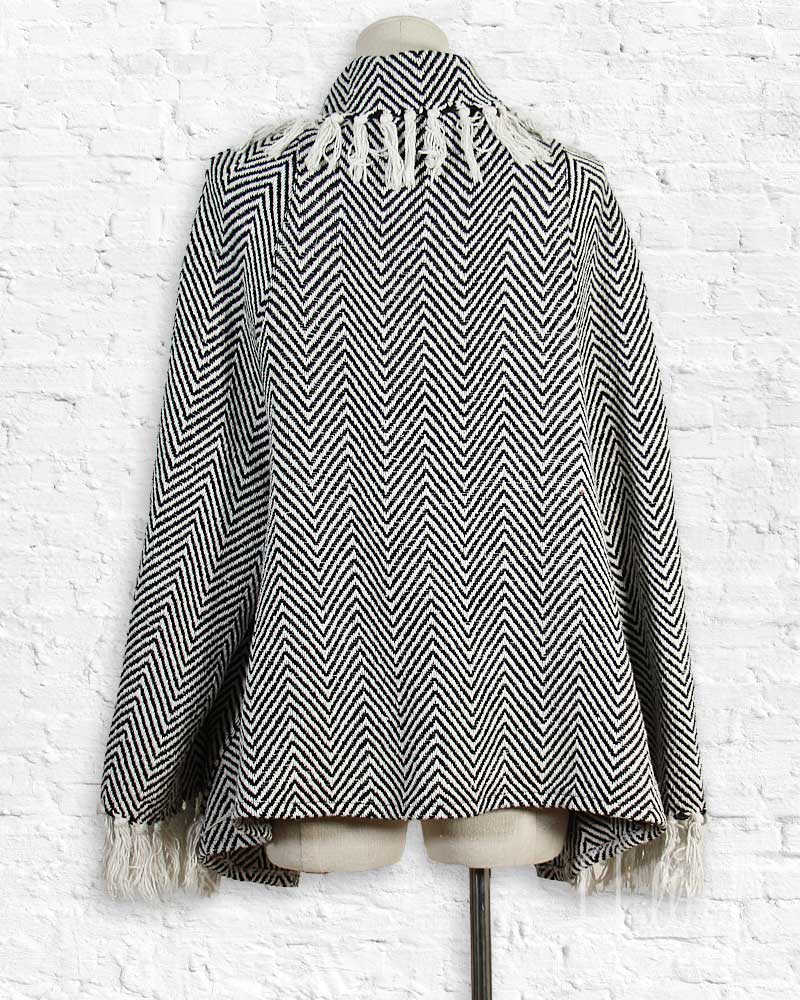 Black and white patterned poncho on a mannequin against a white brick wall.