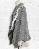 Black and white striped poncho with tassels on a mannequin against a textured white background