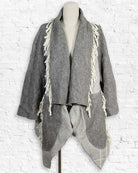 Gray textured jacket with fringe details on a mannequin against a white brick wall.
