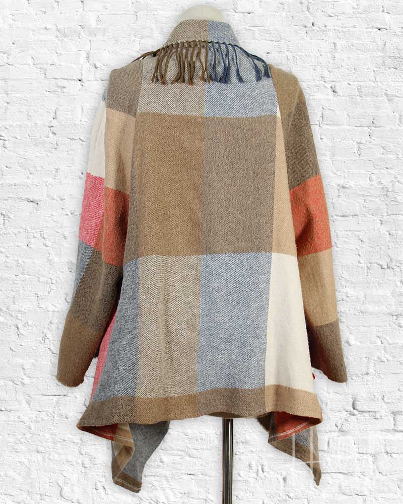 Color-blocked poncho on a mannequin against a white brick wall.