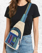 Person wearing a crossbody bag with blue and beige design against a white brick wall.