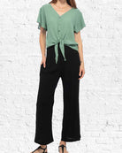 Person wearing a green top and black pants against a white brick wall.
