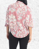 Person wearing a pink floral patterned shirt against a white brick wall.