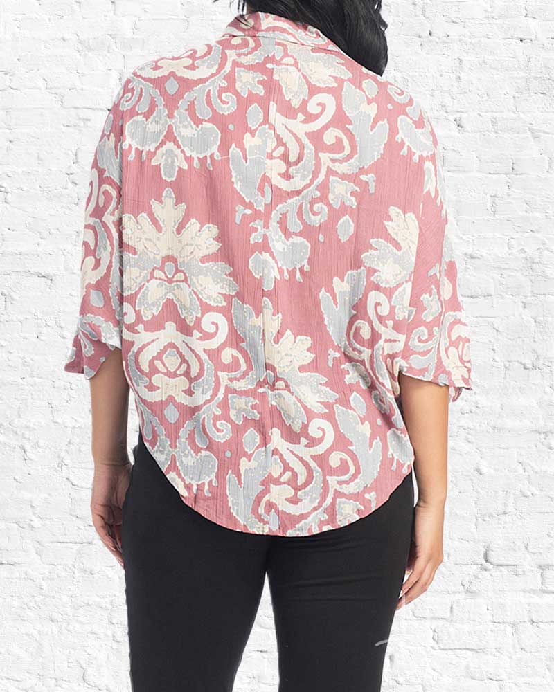 Person wearing a pink floral patterned shirt against a white brick wall.