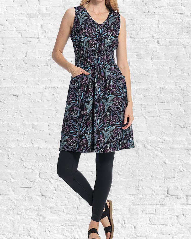 Woman wearing a sleeveless dress with a leaf pattern against a white brick wall.