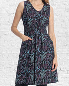 Woman wearing a sleeveless dress with a leaf pattern against a white brick wall.