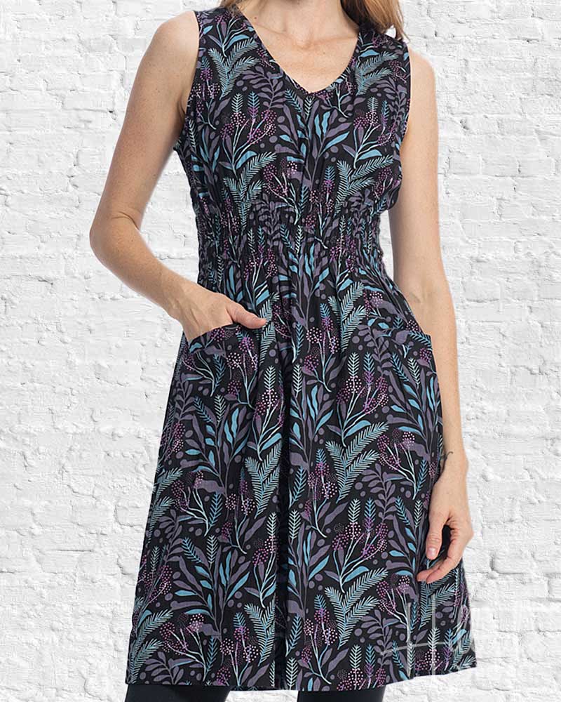 Woman wearing a sleeveless dress with a leaf pattern against a white brick wall.