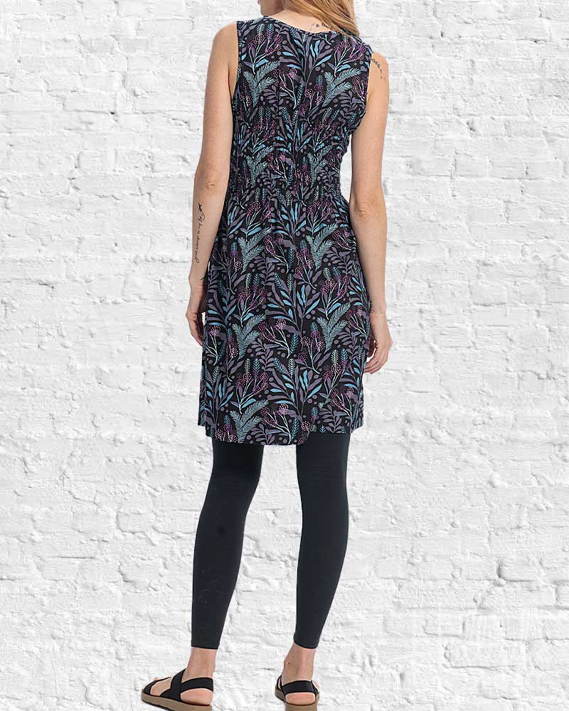 Person wearing a sleeveless dress with a leaf pattern against a white brick wall.