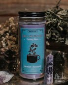 Candle jar with a blue label featuring text and graphics, surrounded by dried plants and crystals.