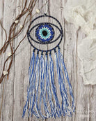 Decorative eye-shaped ornament with blue and white tassels on a wooden background