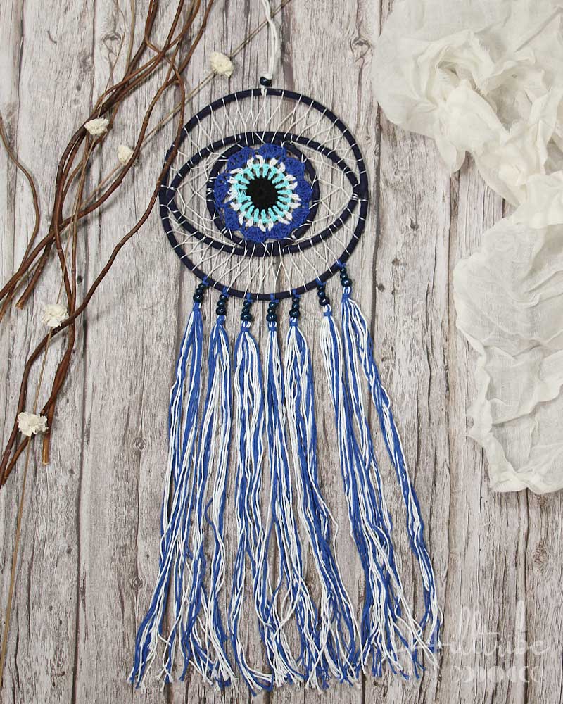 Decorative eye-shaped ornament with blue and white tassels on a wooden background