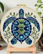 Embroidery hoop with a mosaic turtle design surrounded by green leaves.