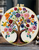 Embroidered tree of life with colorful flowers in a wooden hoop.