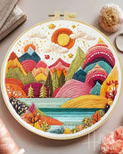 Embroidery hoop with a colorful mountain landscape design on a light background.