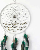 White dreamcatcher with green feathers and small stones on a white background