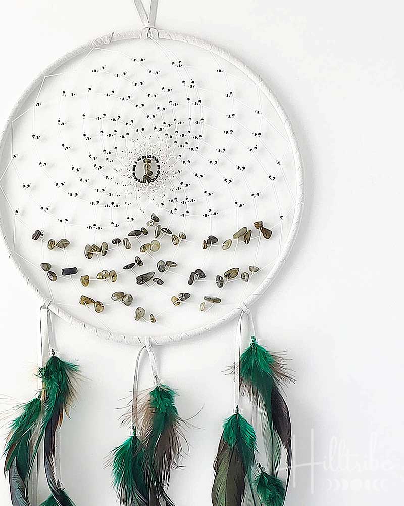 White dreamcatcher with green feathers and small stones on a white background