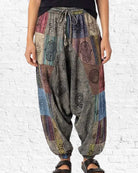 Person wearing colorful patchwork harem pants against a white brick wall.