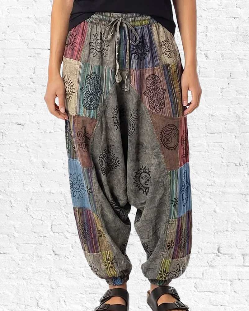 Person wearing colorful patchwork harem pants against a white brick wall.