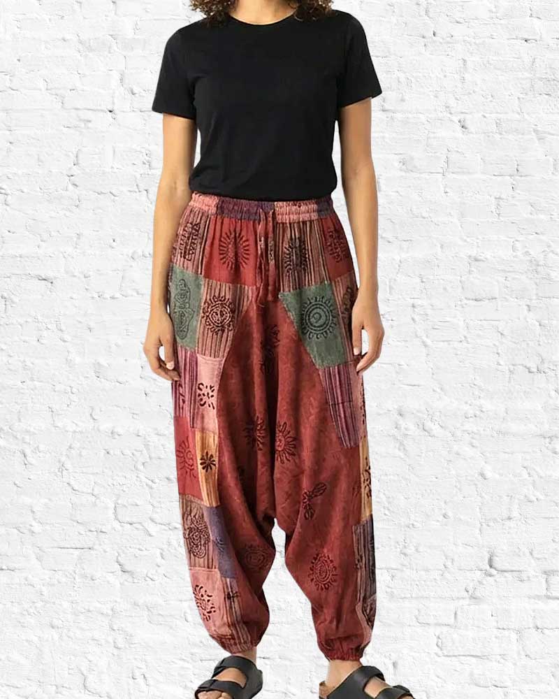 Person wearing a black t-shirt and patterned red harem pants against a white brick wall.