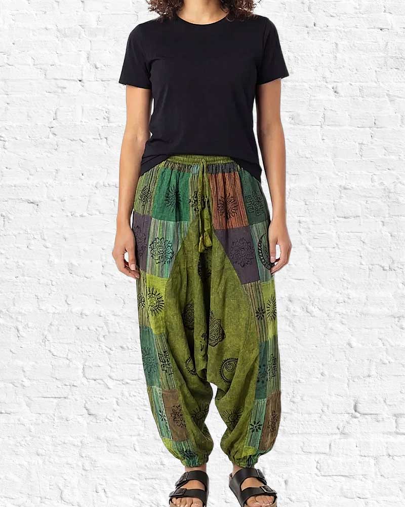 Person wearing a black t-shirt and green patterned harem pants against a white brick wall.