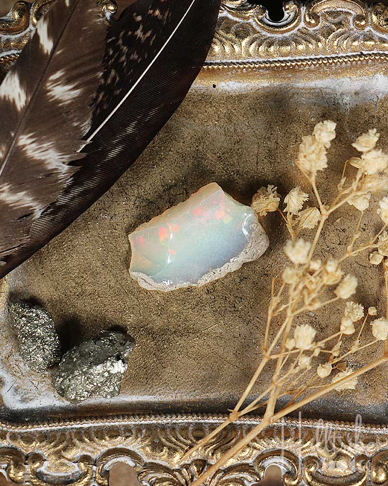 Opal stone with feathers and dried flowers on an ornate surface