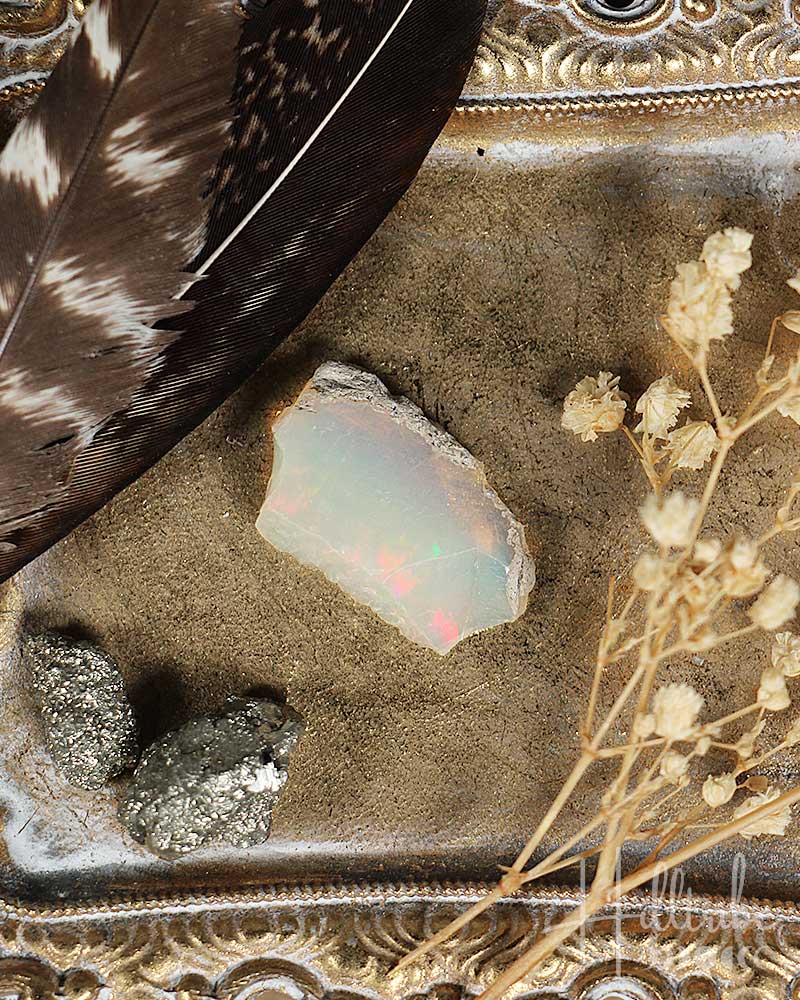 Opal stone with feather and dried flowers on an ornate surface