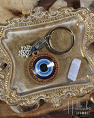 Keychain with evil eye design on a decorative metal tray, featuring the brand 'Hilltribe'.