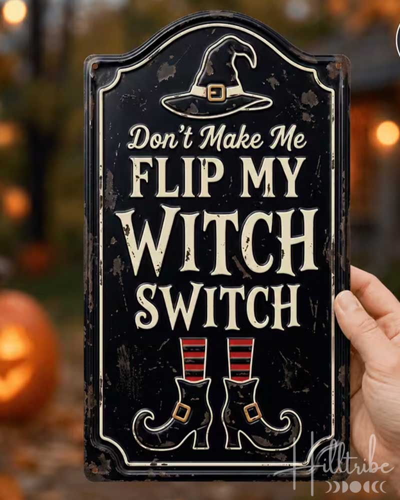 A hand holds a rectangular black decorative sign with a distressed finish. The sign features a witch hat illustration at the top and the phrase 'Don't Make Me FLIP MY WITCH SWITCH' in cream lettering, with witch boot graphics at the bottom.