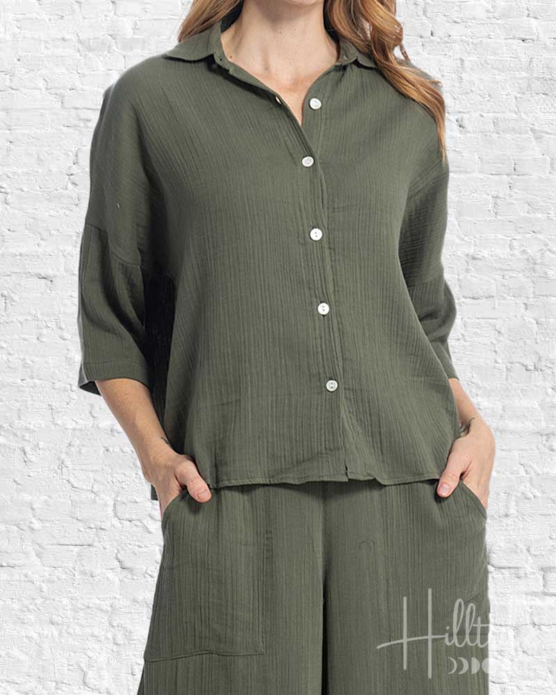 Person wearing a green button-up shirt and wide-leg pants against a white brick wall.