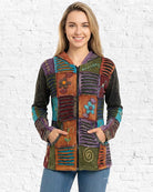 Woman wearing a colorful, patchwork-style jacket against a white brick wall.
