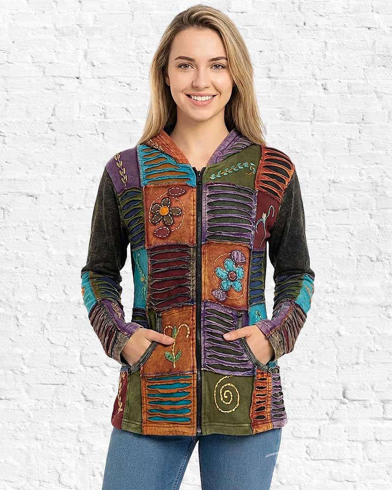 Woman wearing a colorful, patchwork-style jacket against a white brick wall.