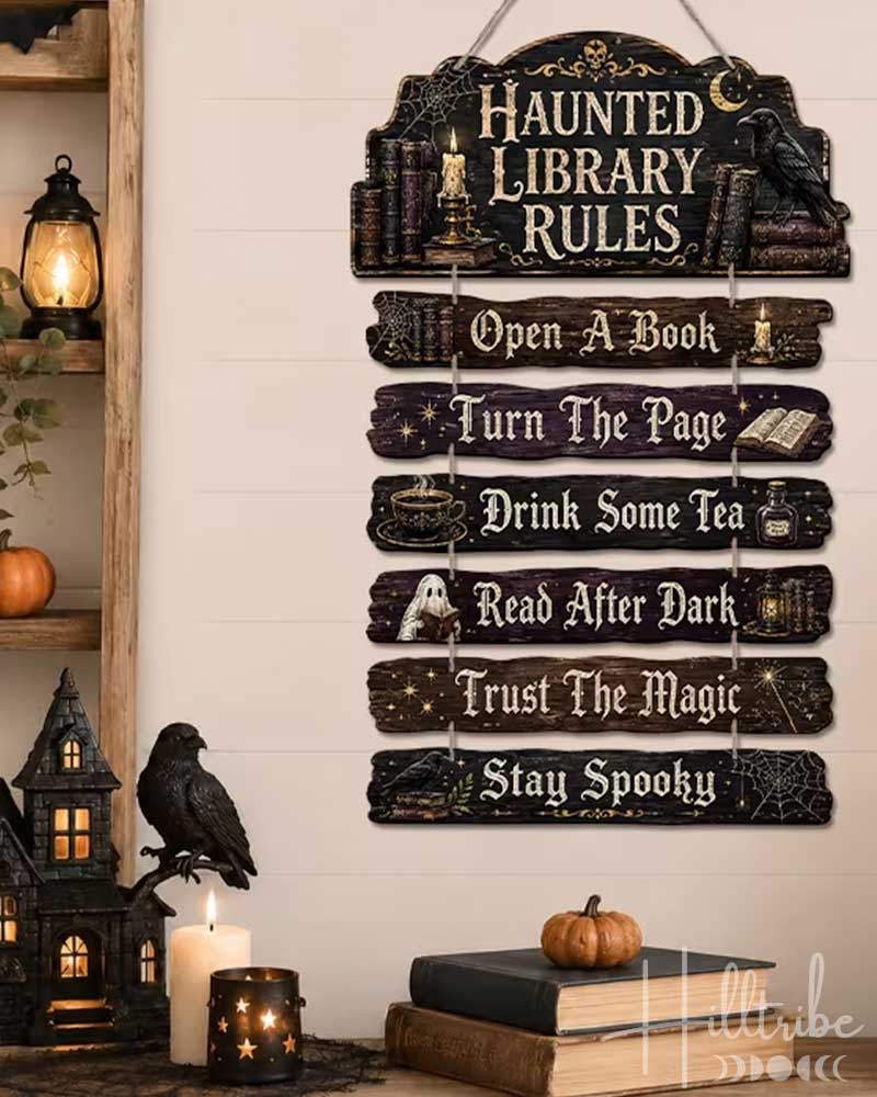 A Halloween-themed wooden hanging sign with the text 'HAUNTED LIBRARY RULES' and nine stacked rules, displayed on a shelf in a decorated room with candles, pumpkins, a house, and bats.