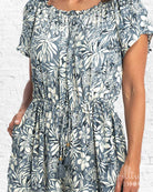 Woman wearing a blue floral dress against a white brick wall.