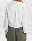 Person wearing a white blouse and green pleated skirt against a white brick wall.