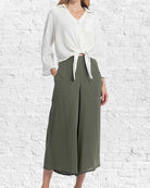 Person wearing a white blouse and green skirt against a white brick wall.