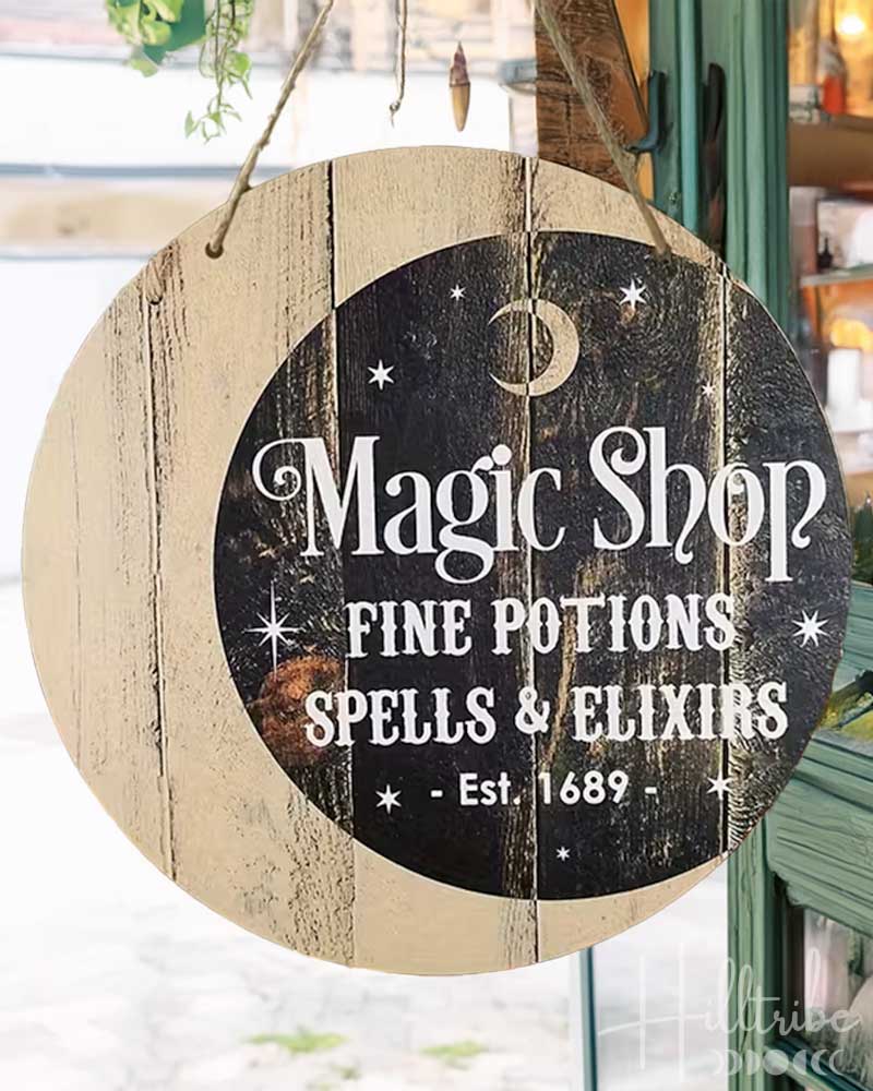 A round hanging wooden sign with a distressed wood-grain border and a dark central panel reading 'Magic Shop Fine Potions Spells & Elixirs Est. 1689' in white lettering, suspended by twine in a room setting.