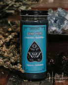 A glass jar candle with a black lid and a turquoise label reading 'DUMP HIM' and 'YES NO', styled on a rustic wooden surface with dried herbs and a crystal in the background.