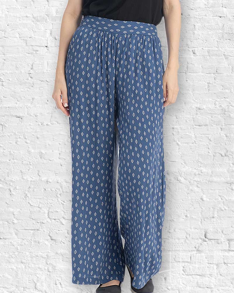 Person wearing blue patterned pants against a white brick wall.