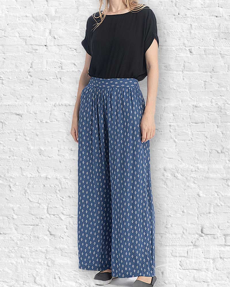 Person wearing a black top and blue patterned pants against a white brick wall.