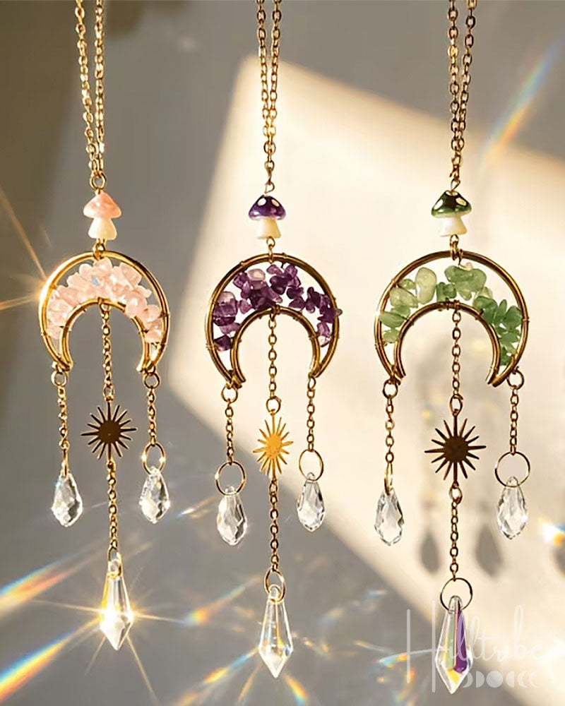 Three gold crescent moon and sun pendant necklaces with dangling crystal teardrops and gemstone accents, shown hanging against a warm light background with lens flare effects.