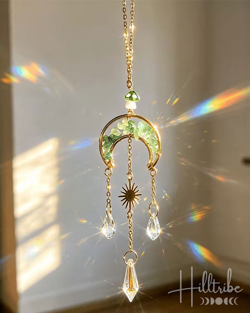 A gold crescent moon suncatcher with green glitter accents, dangling crystal teardrops, and a star charm, shown hanging in warm sunlight with rainbow light leaks on a beige wall.