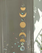 Decorative hanging with gold moon phases and crystal elements against a neutral background